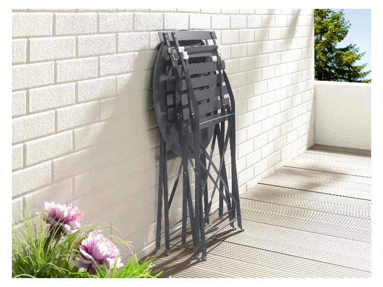 Un ensemble de jardin en métal gris avec une table ronde et deux chaises, contre un mur de briques blanches.