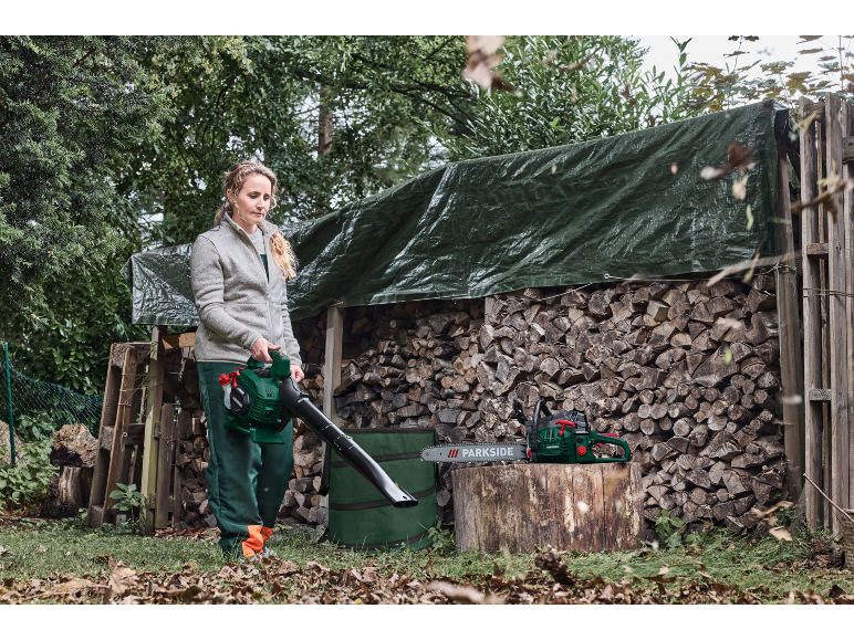 Femme avec souffleur de feuilles Parkside et tronçonneuse près d'un tas de bois.