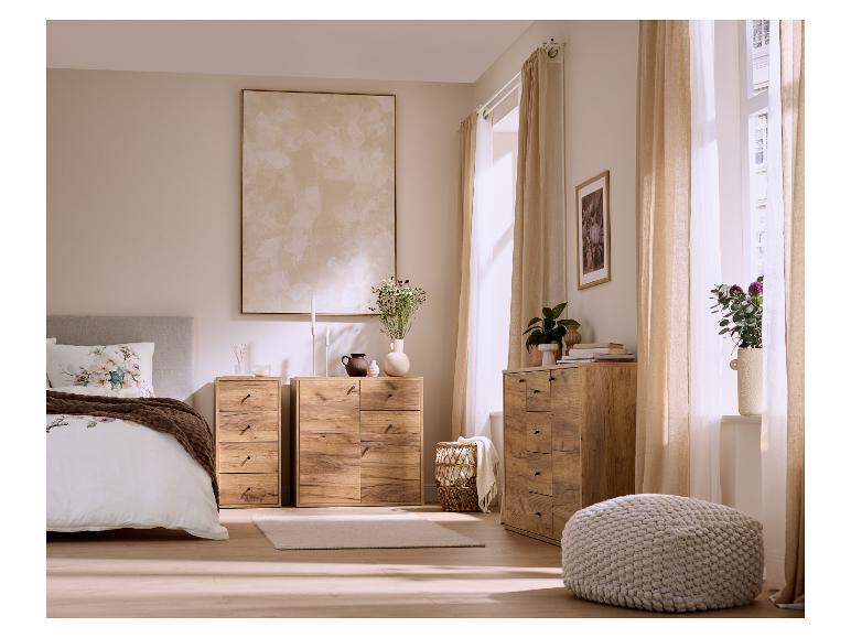 Chambre à coucher avec commodes en bois, un lit avec literie florale et rideaux clairs.