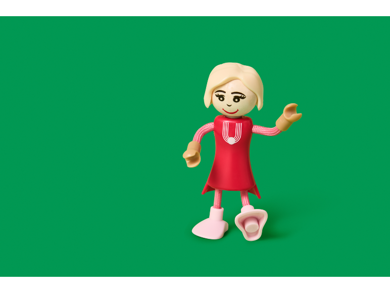 Fille jouet en robe rouge aux cheveux blonds sur fond vert.