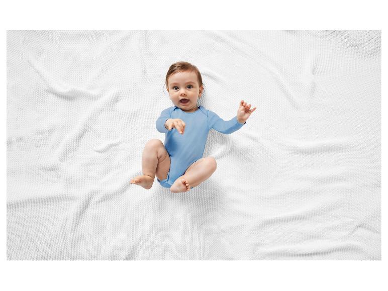 Bébé souriant sur un lange blanc, vêtu d'un body bleu.