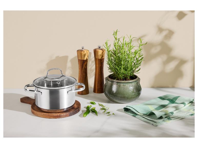 Casserole en acier inoxydable avec couvercle en verre, moulins à sel et poivre en bois et plante de romarin.