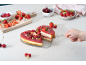 Cheesecake en forme de cœur aux baies, servi avec des fraises, des framboises et des cerises.