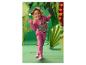 Fille en survêtement rose imprimé dinosaures et baskets, souriante dans un décor de jungle en papier.
