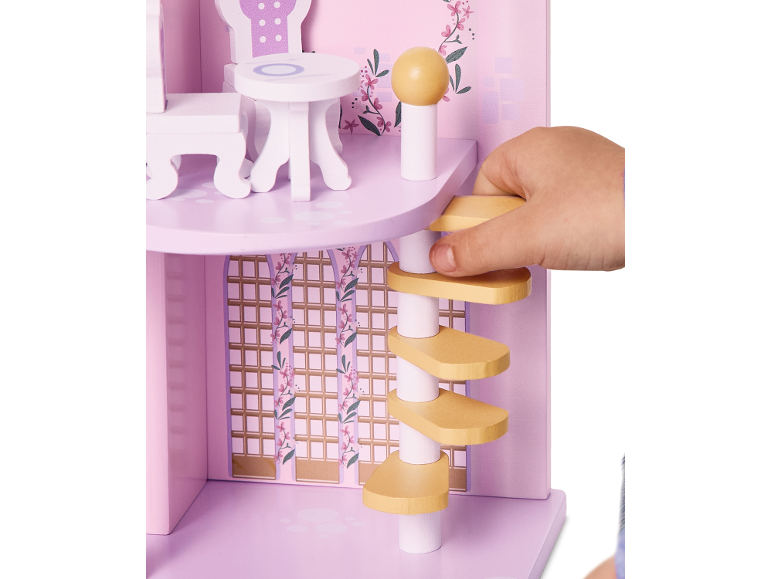 Main d'enfant jouant avec une maison de poupée en bois rose, avec meubles et escalier en colimaçon.