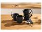 Tasses à café noires empilées sur une table en bois avec des biscuits en arrière-plan.