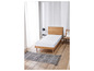 Un matelas blanc sur un cadre de lit en bois avec un tapis gris.