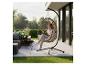 Femme lisant dans un fauteuil suspendu en osier sur la terrasse avec mobilier de jardin et brasero.