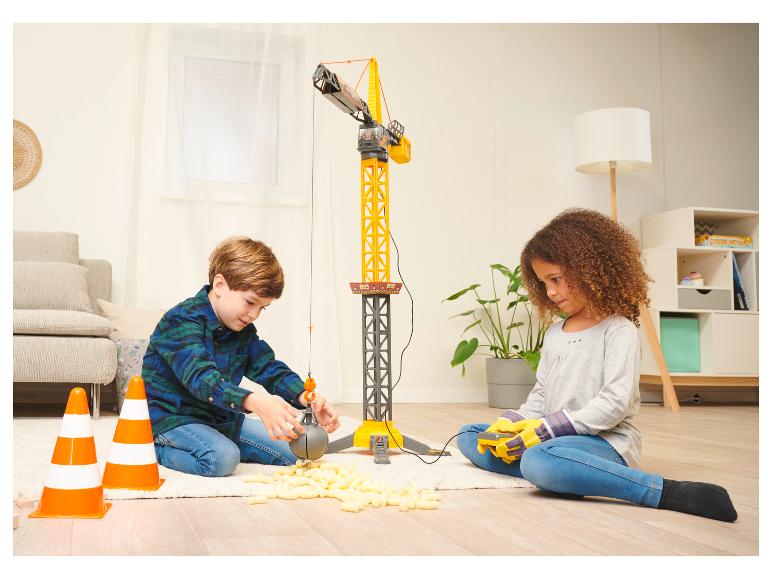 Deux enfants jouent avec une grande grue jouet et des cacahuètes d'emballage sur un tapis.