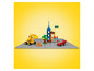 Un excavateur LEGO jaune, une voiture rouge et de petits bâtiments LEGO sur une base grise.