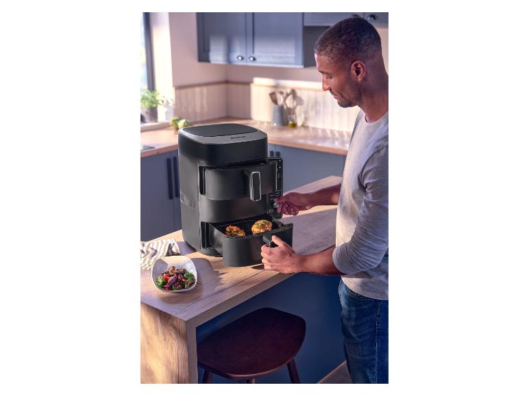 Homme utilisant une friteuse à air noire dans une cuisine, avec un bol de salade à côté.