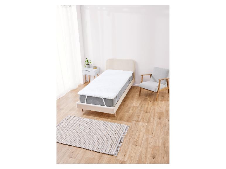 Protège-matelas blanc sur lit simple, avec chaise et tapis.