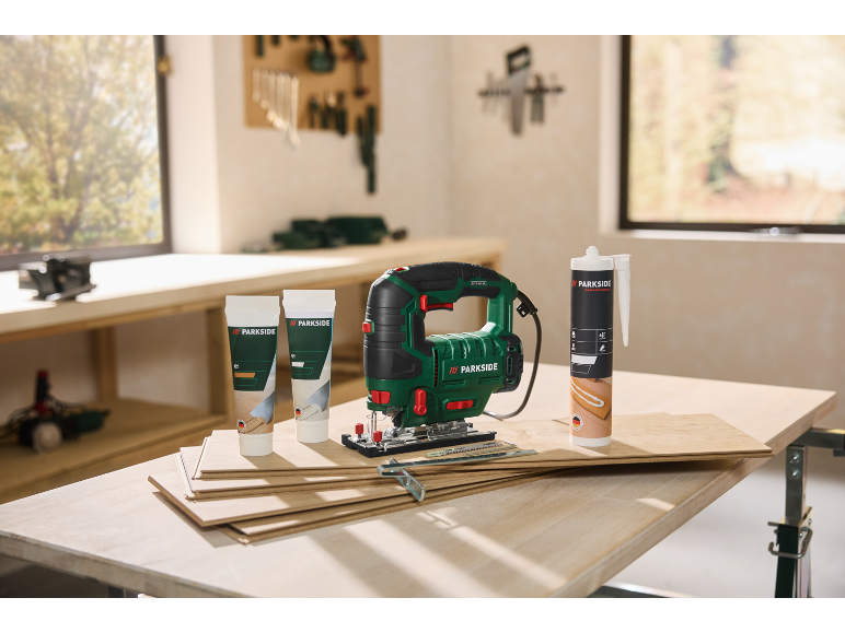 Scie sauteuse, tubes de colle et cartouche de mastic sur des planches en bois sur un établi.