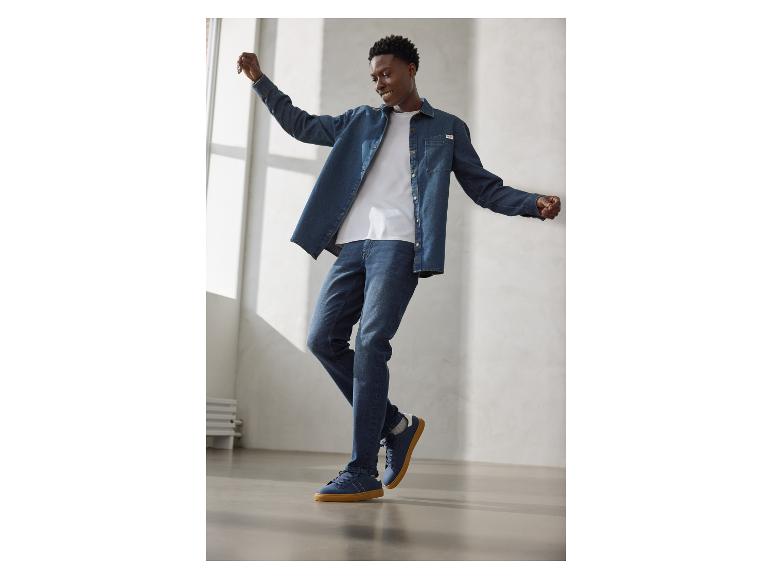 Homme en chemise en jean, t-shirt blanc, jean et baskets bleues à semelle gomme.