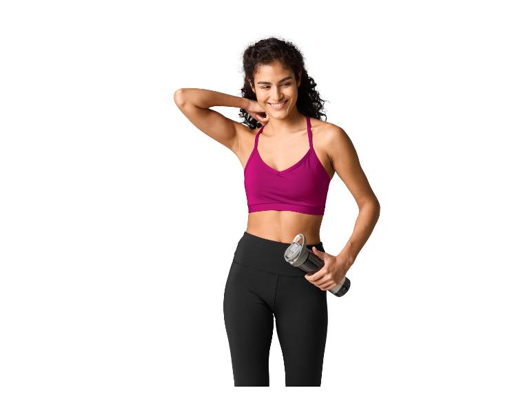Femme en brassière de sport fuchsia et leggings noirs, tenant une bouteille d'eau.