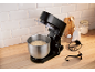 Robot pâtissier noir avec pâte dans un bol en acier inoxydable, sur un comptoir de cuisine en bois.