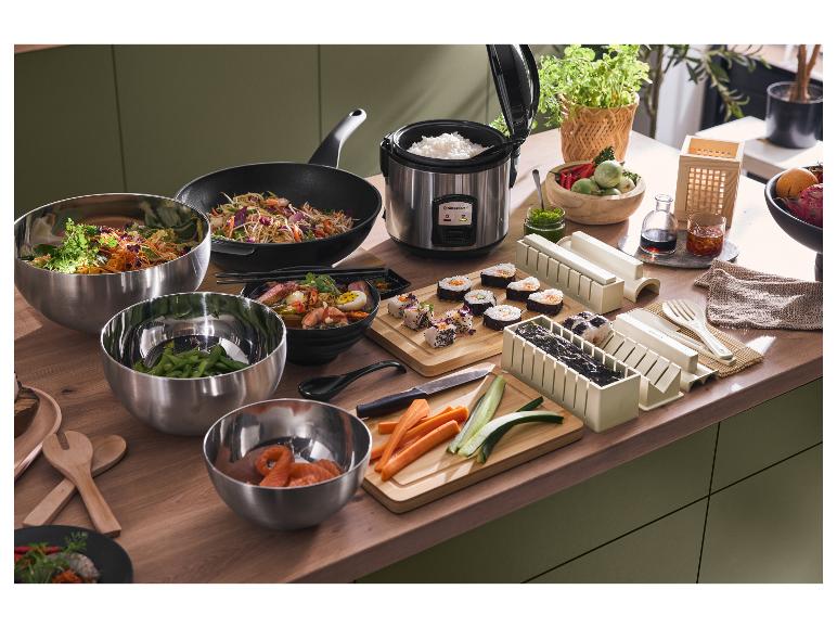 Cuisine asiatique avec cuiseur à riz Silvercrest, wok, moules à sushi et bols sur plan de travail en bois.