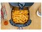 Frites dorées dans une friteuse à air, avec assaisonnements et couverts sur une table en bois.