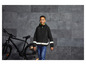 Un garçon portant une veste noire réfléchissante avec une capuche à côté d'un vélo noir.