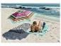 Femme lisant sous un parasol de plage coloré sur un tapis rayé au bord de la mer.