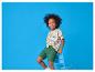 Garçon en t-shirt dinosaure et short vert, souriant sur une chaise bleue.