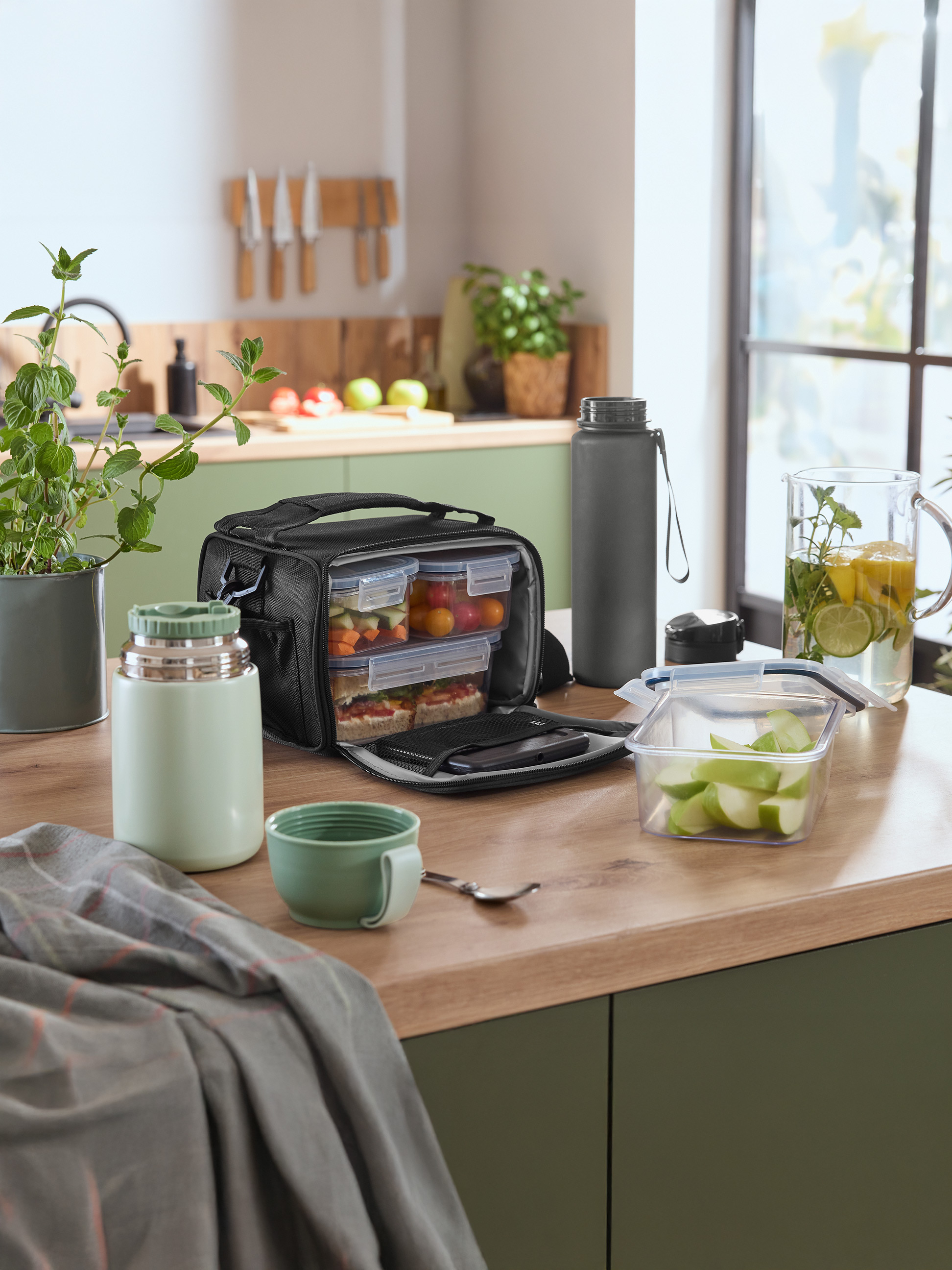 Sac-repas avec boîtes alimentaires, thermos et bouteille d'eau sur un comptoir de cuisine.