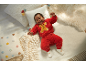Bébé souriant dans un ensemble en peluche rouge avec un bonhomme de pain d'épice, allongé sur des coussins.