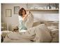 Femme en pyjama vert clair faisant son lit avec une couette et des oreillers beiges.