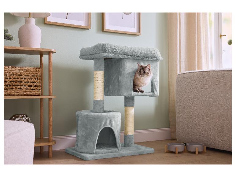 Un chat dans un arbre à chat gris, à côté d'une étagère en bois et de gamelles pour animaux.