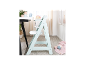 Chaise haute en bois bleu clair avec plateau, à côté d'une table avec des articles pour bébé.