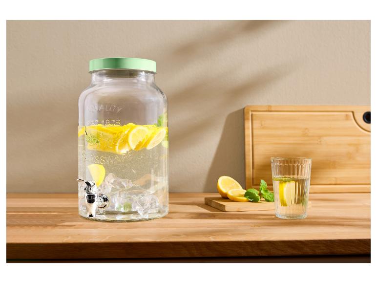 Distributeur de boissons en verre avec citrons et menthe, verre d'eau avec citron sur une table en bois.