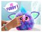 Furby violet avec des accents bleus et des yeux roses, touché par un enfant, avec une bulle de dialogue 'HÉ FURBY!'
