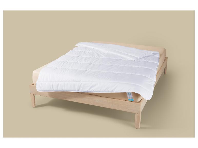 Couette blanche matelassée sur un cadre de lit en bois clair avec un matelas beige