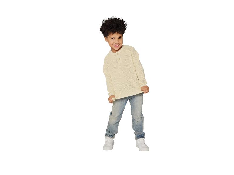 Garçon souriant en pull gaufré crème, jean bleu clair et baskets blanches.