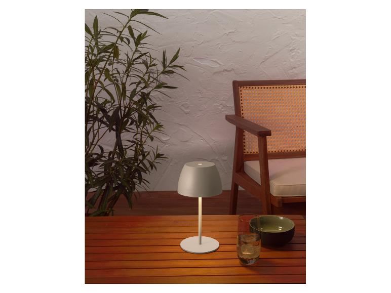 Lampe de table portable sur une table en bois extérieure avec plantes et chaise.