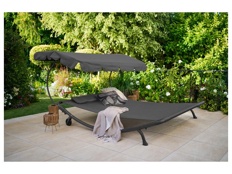 Bain de soleil suspendu gris avec auvent, coussins et plaid sur une terrasse ensoleillée.