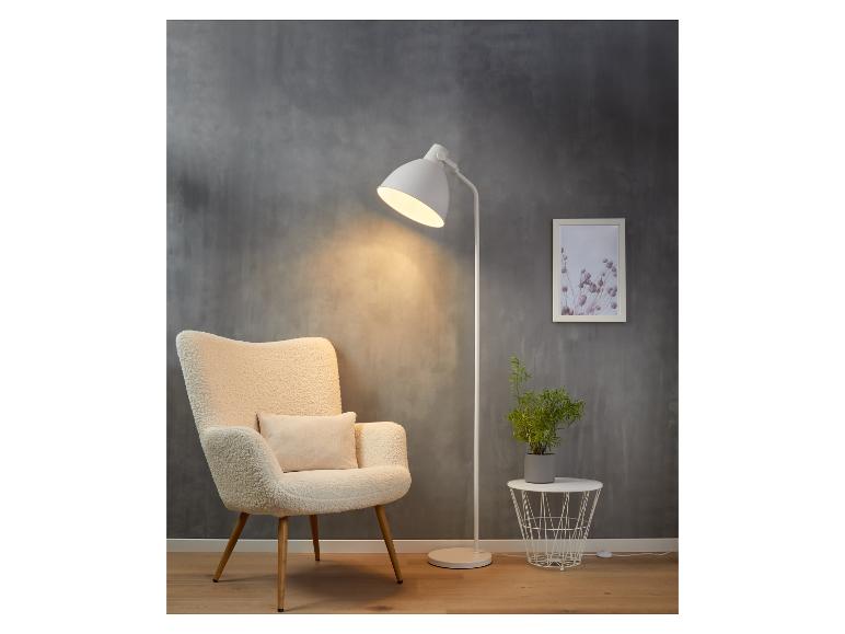 Un lampadaire blanc avec un fauteuil, une plante et une table d'appoint.