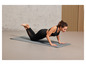 Une femme en brassière de sport et leggings fait des pompes sur un tapis de yoga gris.