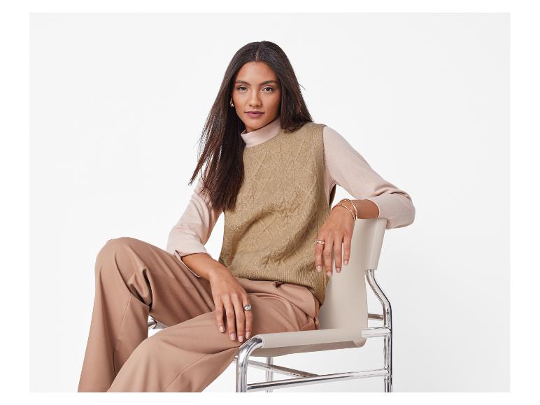 Femme en gilet tricoté beige et pantalon assorti, assise sur une chaise moderne.
