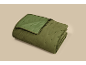 Jeté de lit matelassé vert olive plié avec motif sur fond neutre.