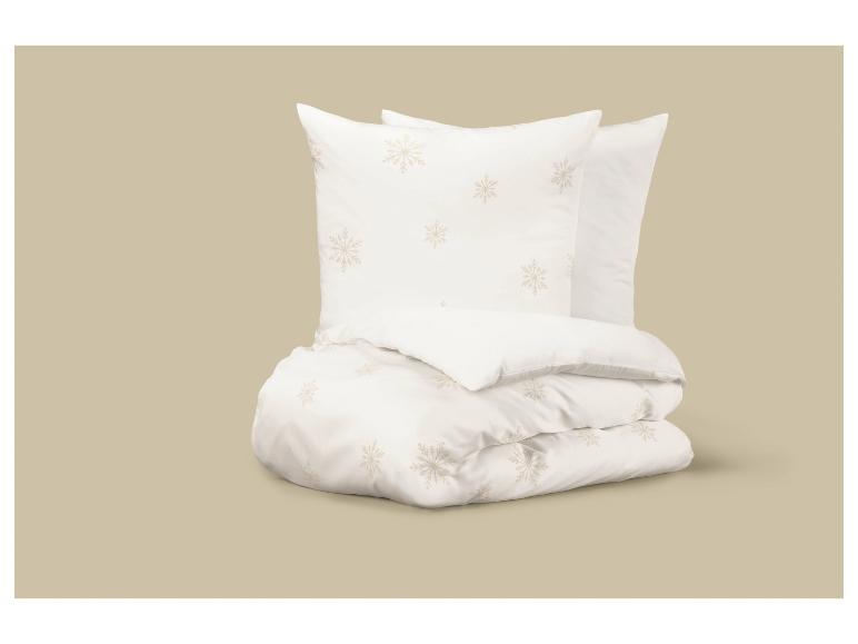 Parure de lit blanche avec des flocons de neige beiges, pliée sur un fond beige.