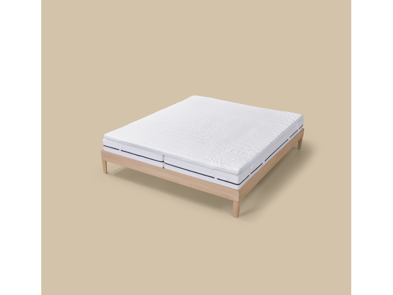 Un cadre de lit en bois clair avec deux matelas blancs et un surmatelas blanc.