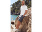 Un homme porte un polo blanc, un short gris et des baskets blanches sur la côte.