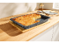 Un plat de cuisson avec un gâteau aux amandes sur un comptoir en bois, avec une part coupée.