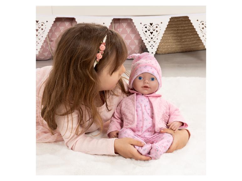 Fille jouant avec une poupée bébé en tenue rose sur un tapis blanc.