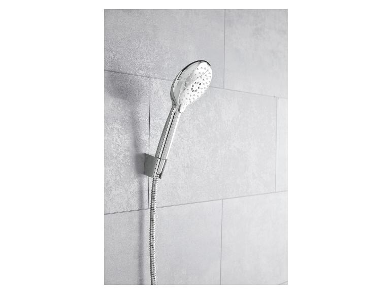 Pomme de douche et flexible chromés, installés sur un mur de carreaux gris.