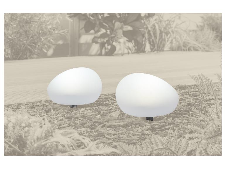 Deux lampes de jardin blanches en forme d'œuf sur du paillis avec des plantes en arrière-plan.