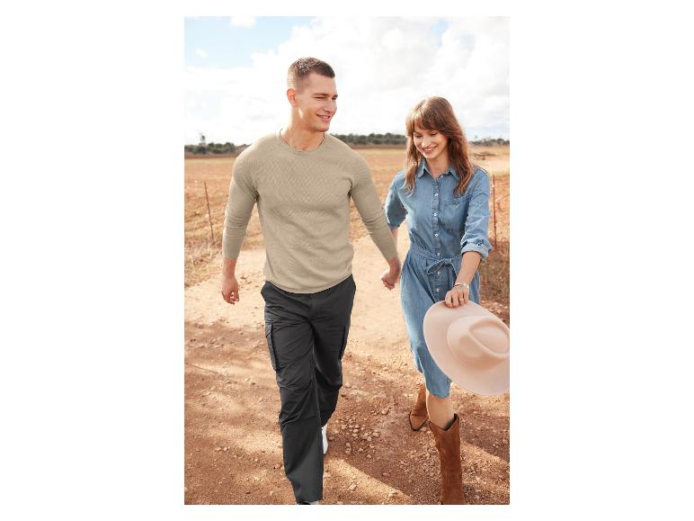 Un homme et une femme marchent main dans la main sur un chemin de terre, elle porte une robe en jean et des bottes de cow-boy.