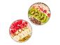 Deux bols de yaourt avec différentes garnitures, dont des framboises, une banane, du muesli, du kiwi et une pomme.