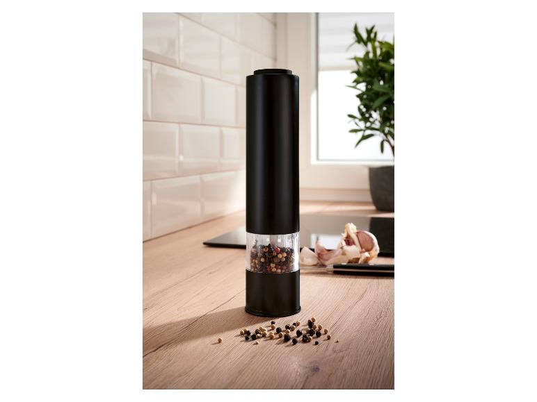 Moulin à poivre électrique noir avec grains de poivre sur un comptoir de cuisine en bois.